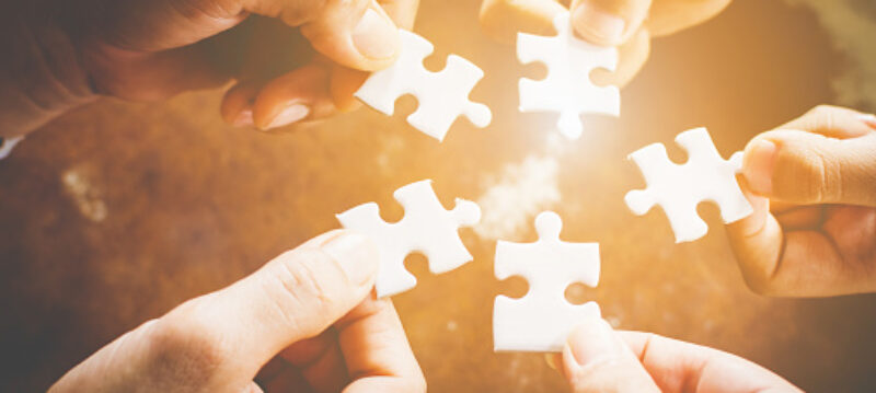 Comment_travailler_avec_une_équipe_délocalisée Hand of diverse people connecting jigsaw puzzle. Concept of partnership and teamwork in business